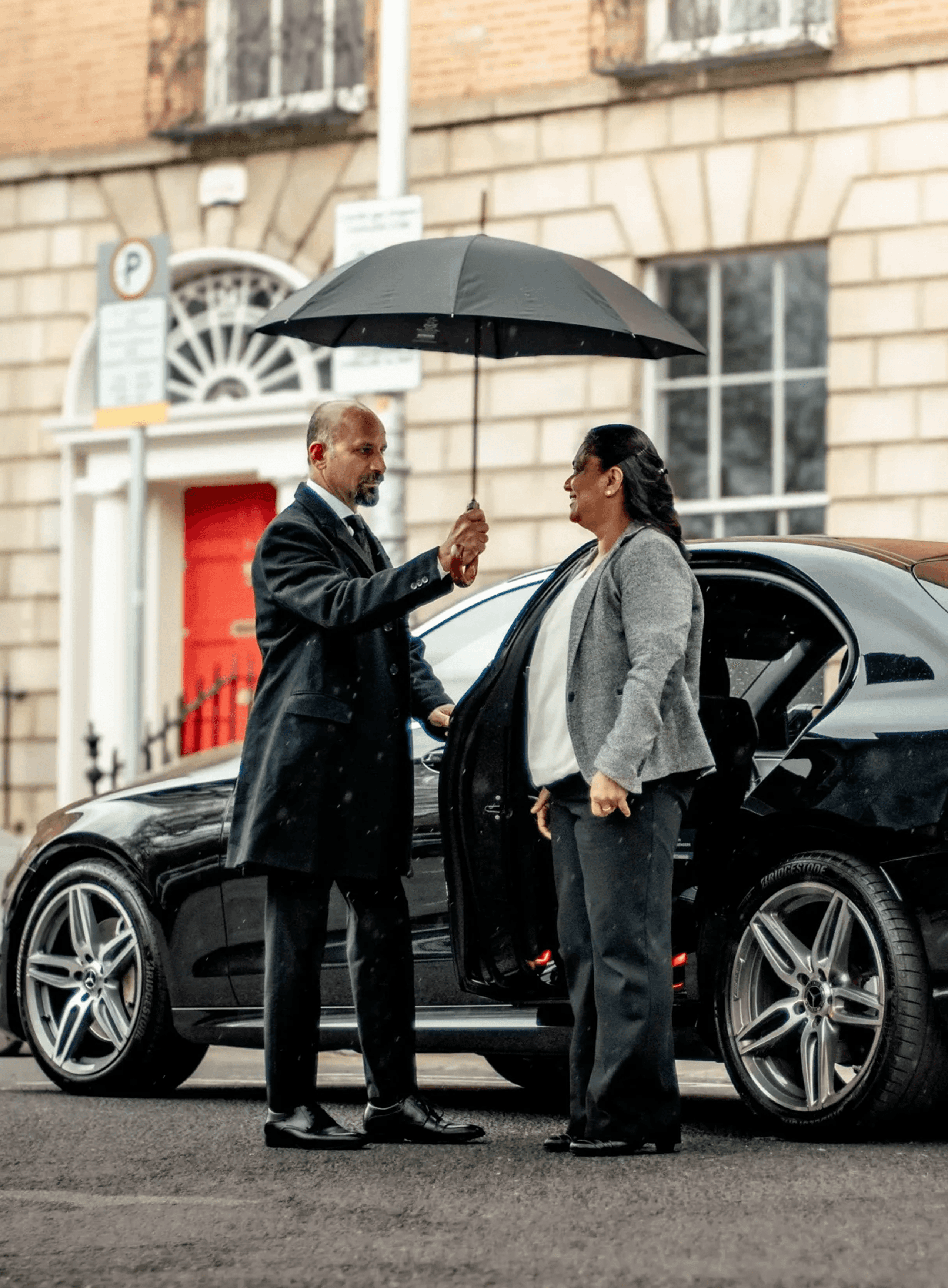 Chauffeur holding an umbrella for a client beside a black car