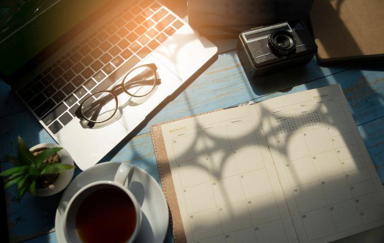 A laptop, calendar, cup of tea and a camera on a desk