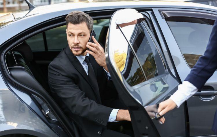 A man being let out of the car while a chauffeur opens the door