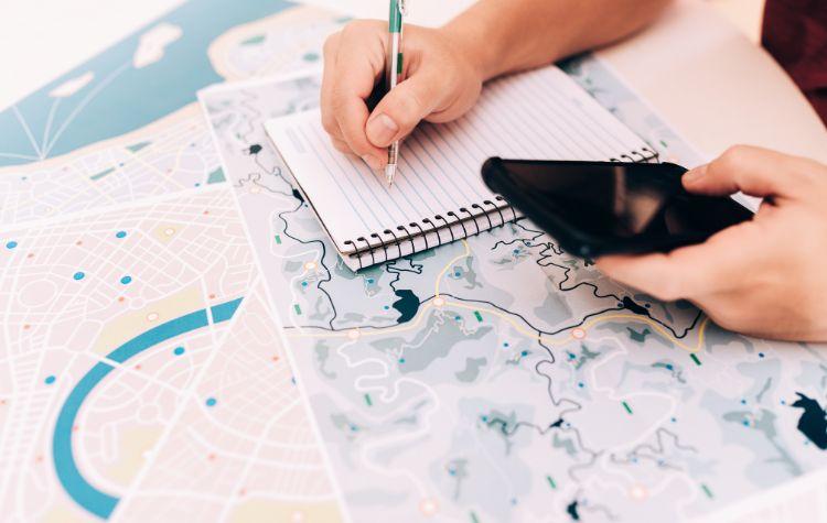 Person filling out a notebook on top of a map