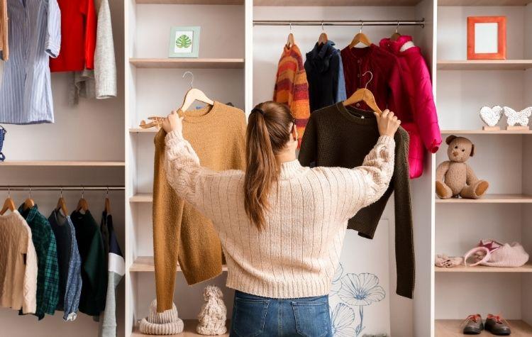 Person in closet choosing between two sweaters