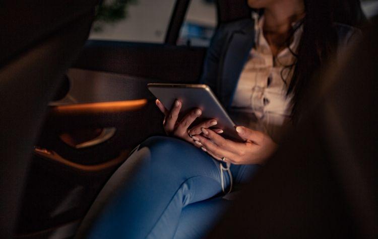 Woman sitting in the back of a car holding a tablet